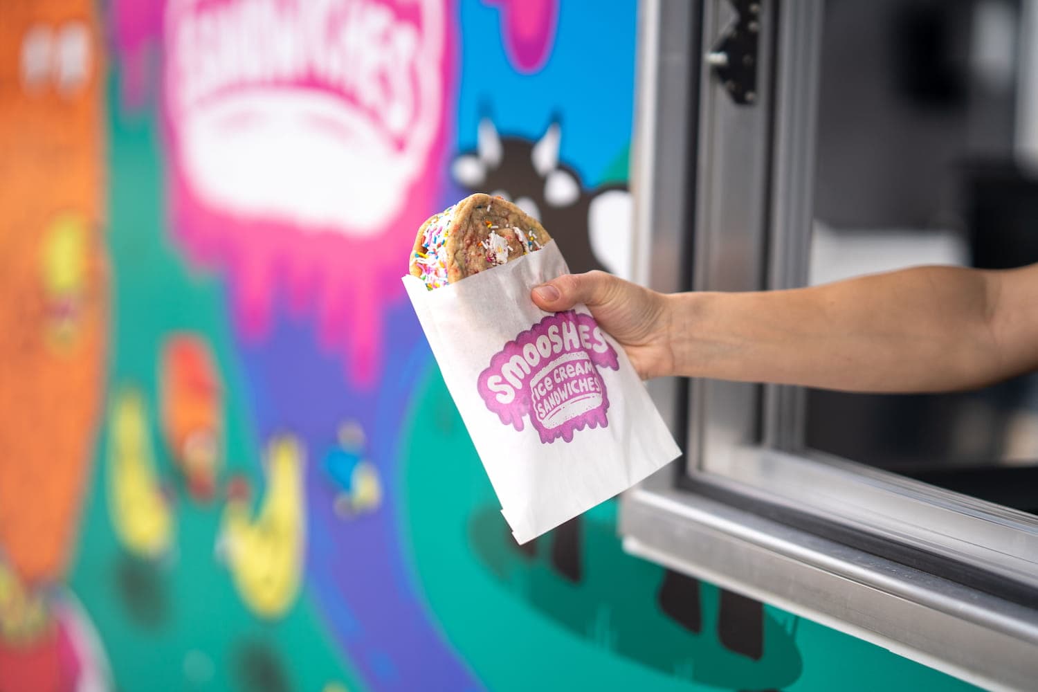 Hand holding out an ice cream sandwich out the window of the Smooshies food truck.