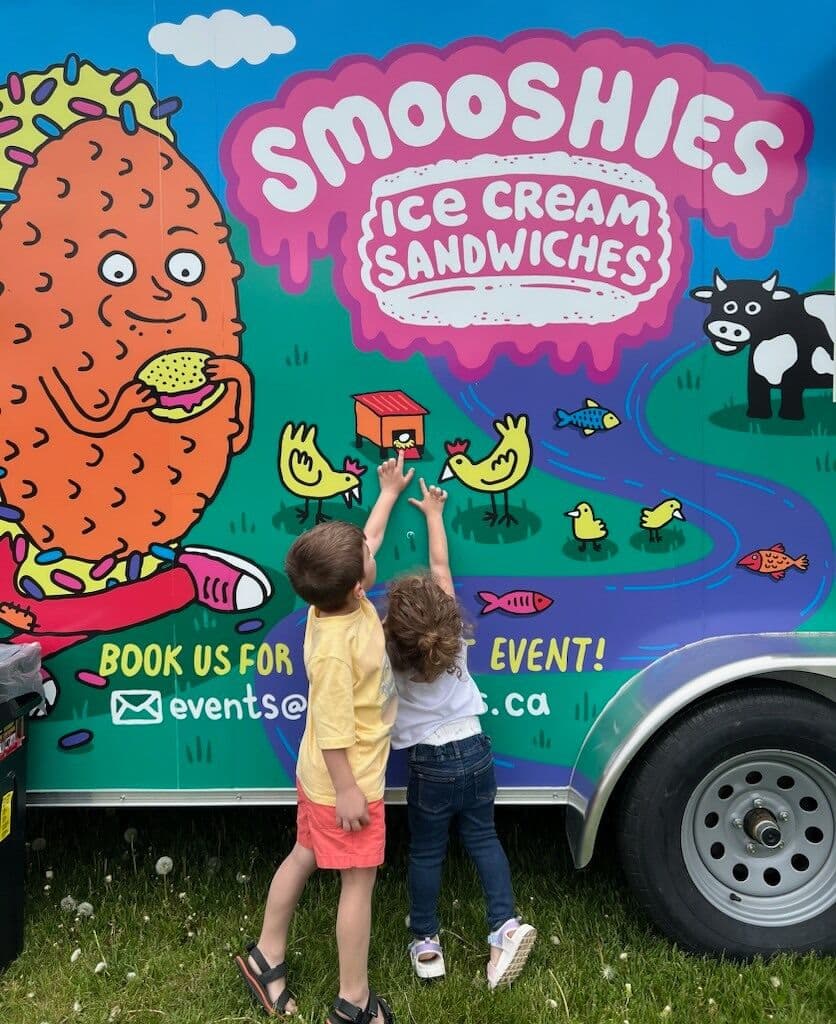 Two young children pointing at the Smooshies food truck artwork.