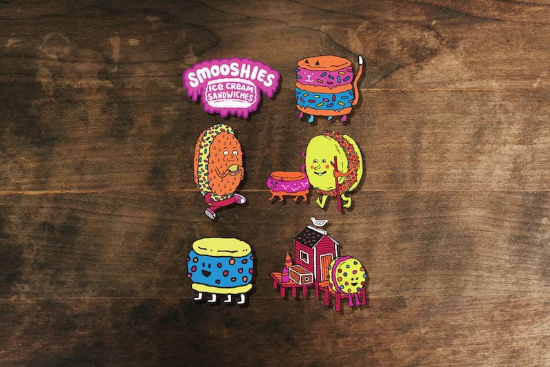 Collection of vinyl Smooshies artwork stickers spread out on a wood table.