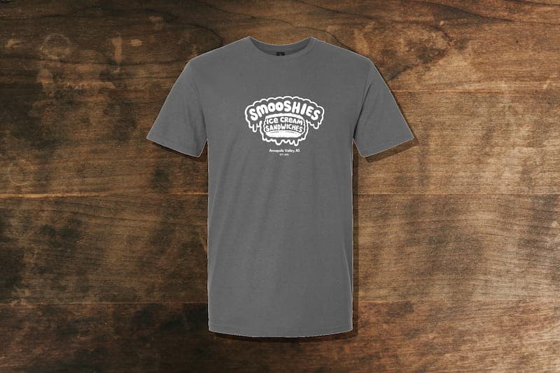 Smooshies branded t-shirt spread accross a wood table.